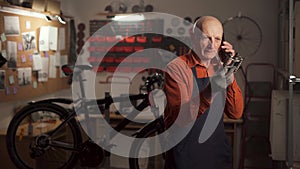 Mature man repairing Bicycle in workshop and calling on cellphone with pedal in hand. bike mechanic in garage. Bike