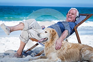 Mature man resting on a deck chair listening to music petting his dog
