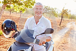 Mature Man Riding Motor Scooter Along Country Road