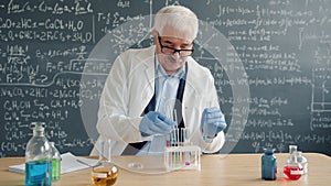Mature man scientist conducting chemical test in laboratory taking notes