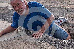 Mature man or senior walking in a building zone and falling in a big hole with her leg inside it - needing help on the ground with photo