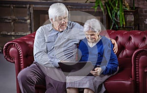 Mature man and senior woman using laptop while sitting on couch