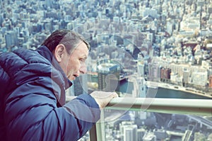 Mature man shaking with fear looking at the panorama of a big city from above