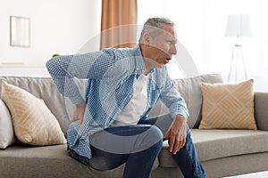 Mature man with side back pain sitting on couch at home