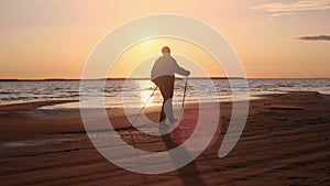 Mature man silhouette Scandinavian walking stick sunset sea sand beach activity healthy lifestyle