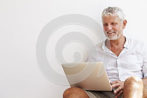 Mature Man Sitting Against Wall Using Laptop