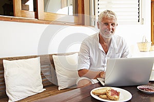 Mature Man Sitting At Breakfast Table Using Laptop