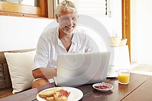 Mature Man Sitting At Breakfast Table Using Laptop