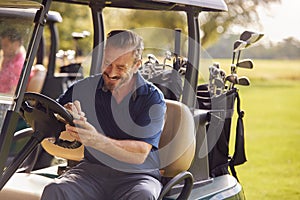 Mature Man Sitting In Buggy Playing Round On Golf And Checking Score Card