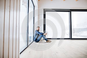 A mature man sitting on the floor in unfurnished new house, holding coffee.
