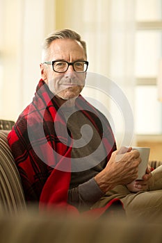 Mature man sitting on a sofa drinking coffee.