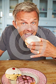 Mature Man Sitting At Table Eating Sugary Donut photo