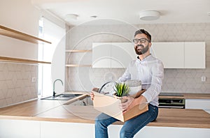 Mature man sitting in unfurnished house, holding a moving box.
