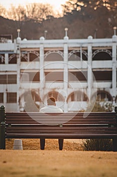 Mature man sitting on a wooden bench overlooking a modern industrial building