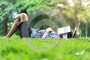 Mature man sleeping on green grass in city park with a book cov