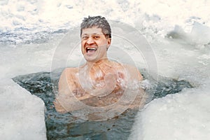 Mature man smiles and bathes in a winter ice hole