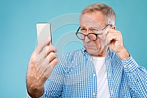Mature man squinting using mobile phone, looking at screen photo