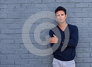 Mature man standing against gray wall with arms crossed