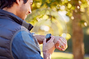 Mature Man Standing By Trees In Autumn Park Looking At Smart Watch