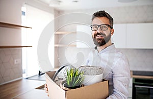 Mature man standing in unfurnished house, holding a moving box.