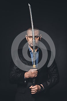 mature man in suit holding japanese katana sword in front of his face