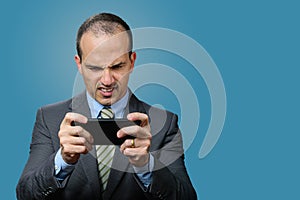 Mature man with suit and tie, playing on his smartphone and gritting his teeth. Blue background