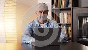 Mature man surfing internet on laptop computer, sitting at cabinet at home