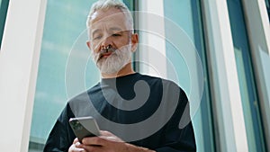 Mature man swiping smartphone on street closeup. Smiling senior with piercing