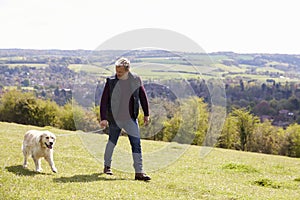 Mature Man Taking Golden Retriever For Walk In Countryside