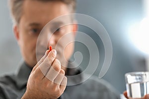 Mature man taking pill on blurred background