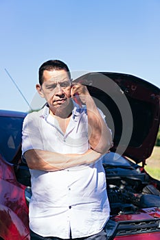 Mature Man talking on cell phone next to broken car