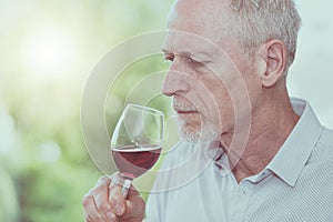 Mature man tasting red wine, light effect