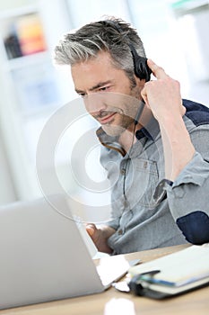Mature man teleworking on laptop using headphones photo