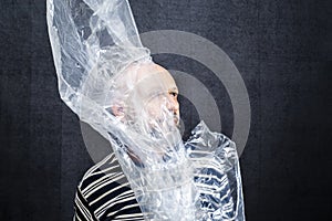 Mature man with a transparent plastic bag flying over his head and face