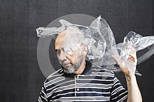 Mature man with a transparent plastic bag flying over his head and face