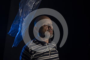 Mature man with a transparent plastic blue bag flying over his head and face