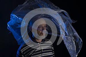 Mature man with a transparent plastic blue bag flying over his head and face