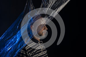 Mature man with a transparent plastic blue bag flying over his head and face