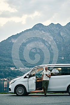 Mature man traveler standing near camper van using mobile in nature park.