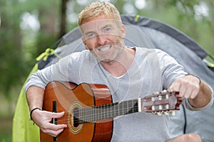 mature man tuning guitar by tent