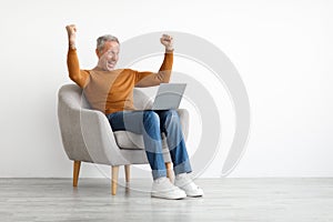 Mature man using laptop celebrating success shaking fists screaming yes