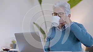 Mature man using laptop while drinking coffee in living room