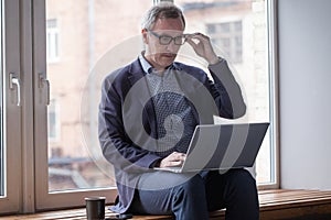 Mature man using laptop indoor. Smiling middle aged businessman in glasses