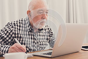 Mature man using laptop and writing in notepad
