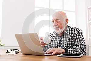 Mature man using laptop and writing in notepad