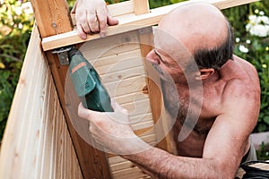 Mature man using power drill building something at contryhouse