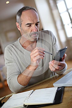 Mature man using smartphone and laptop at home