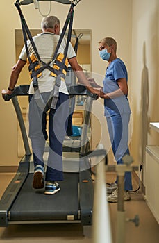 Mature man using treadmill for walking in rehabilitation center