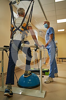 Mature man walking in parallel bars at rehabilitation room