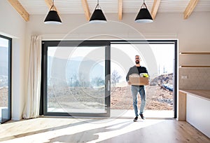 Mature man walking in unfurnished house, holding a moving box.